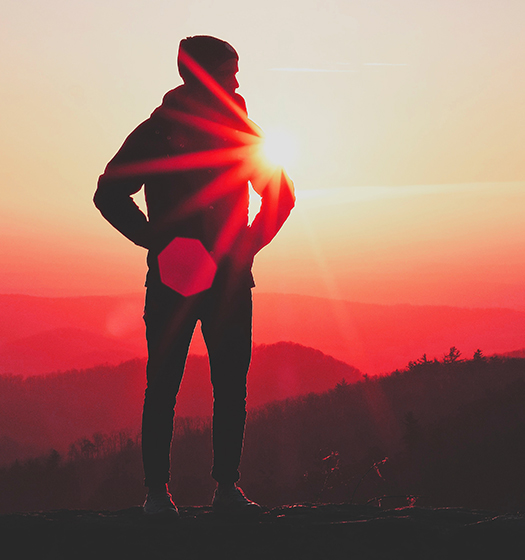 Une personne debout sur une montagne avec le soleil derrière elle