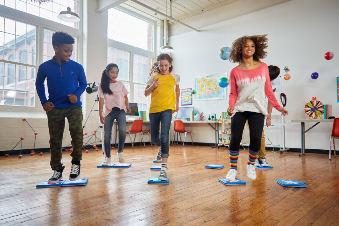 Four children in a classroom, jumping on programmable floor buttons