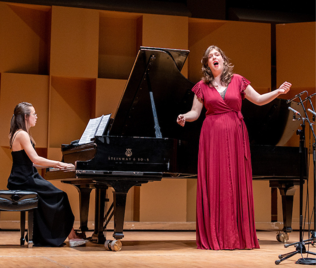 Individuals on stage, one singing and one playing the piano