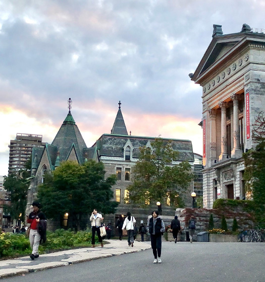 Une douzaine d’étudiants se promènent à l’extérieur devant des bâtiments du campus du centre-ville de McGill.