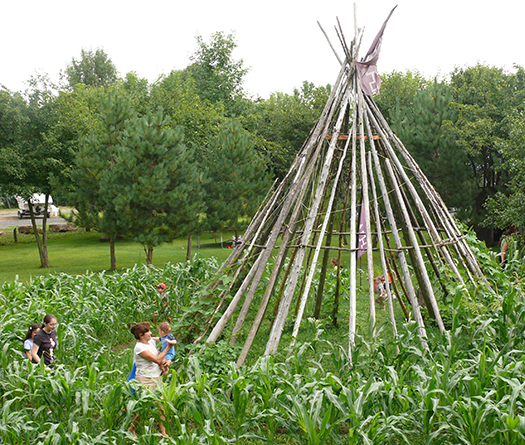 Un groupe de personnes debout dans un champ de plantes avec un tee pee au milieu.