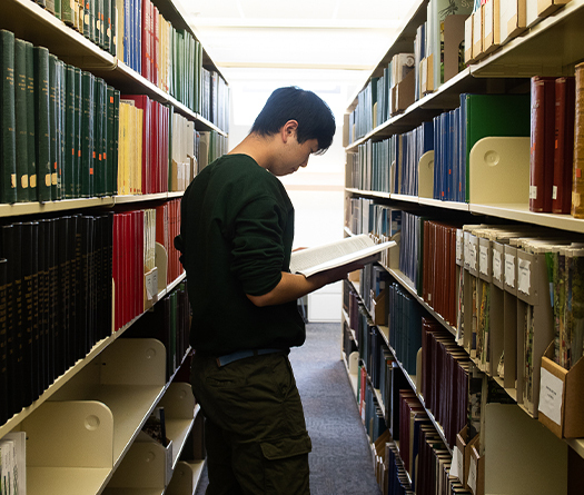Un étudiant debout dans une bibliothèque regardant un livre