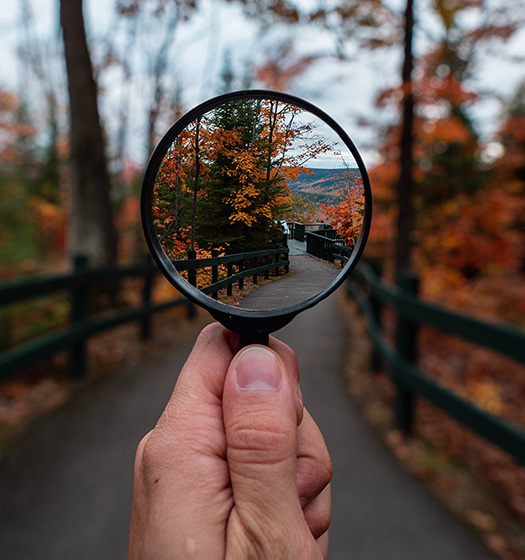 Une main tenant une loupe sur un chemin dans une scène automnale en plein air
