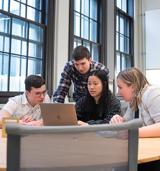 Groupe de quatre étudiants de McGill dans une salle de classe avec de grandes fenêtres, regardant un ordinateur portable.