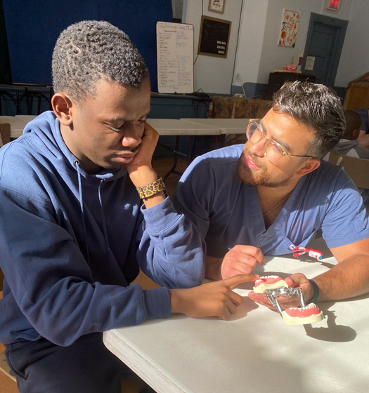 Un étudiant assis à une table avec un professeur lui montrant un modèle d'enseignement des dents.
