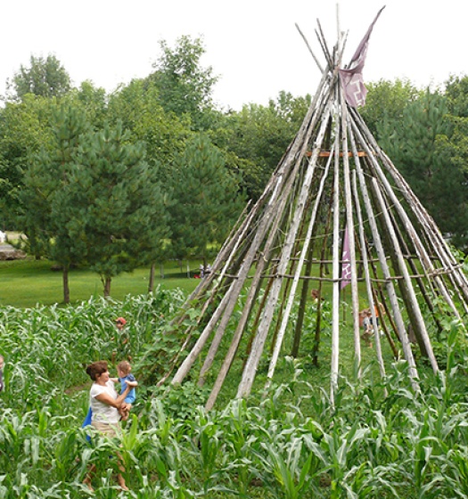 Un groupe de personnes debout dans un champ de plantes avec un tee pee au milieu.