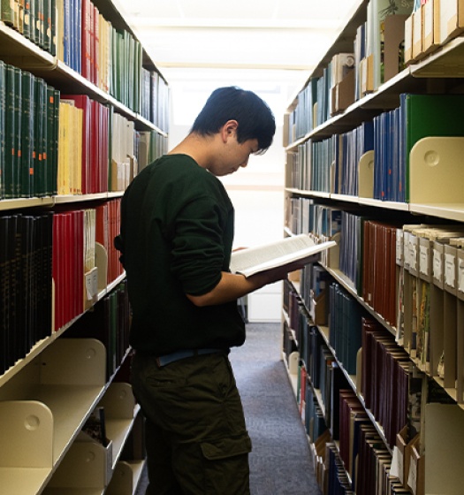 Un étudiant debout dans une bibliothèque regardant un livre