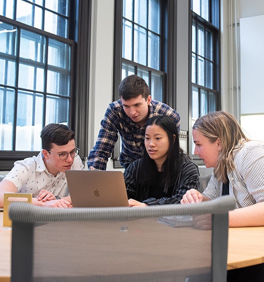 Groupe de quatre étudiants de McGill dans une salle de classe avec de grandes fenêtres, regardant un ordinateur portable.